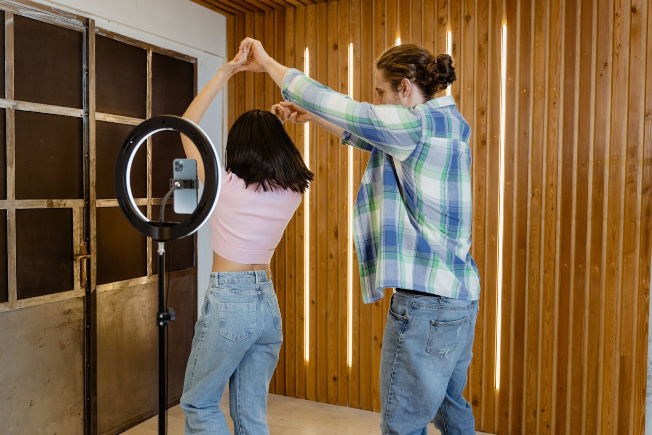 A young couple dances indoors with a ring light recording them, capturing a lively moment.